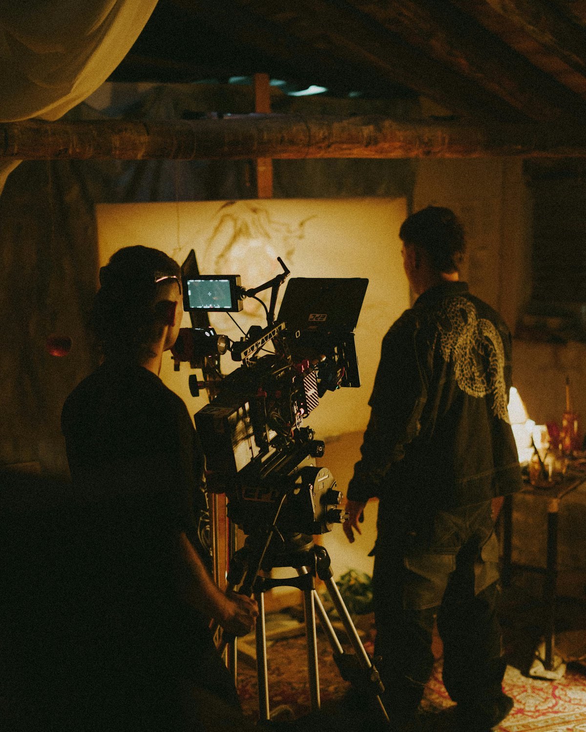 Two crew members working a cinema camera on a warm-lit set