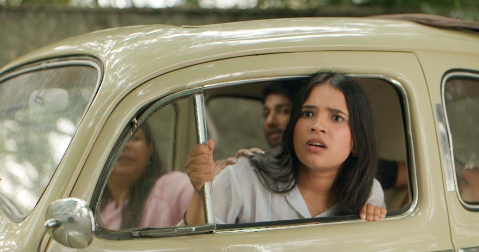 A woman leans out of a vintage car window, mid-scene