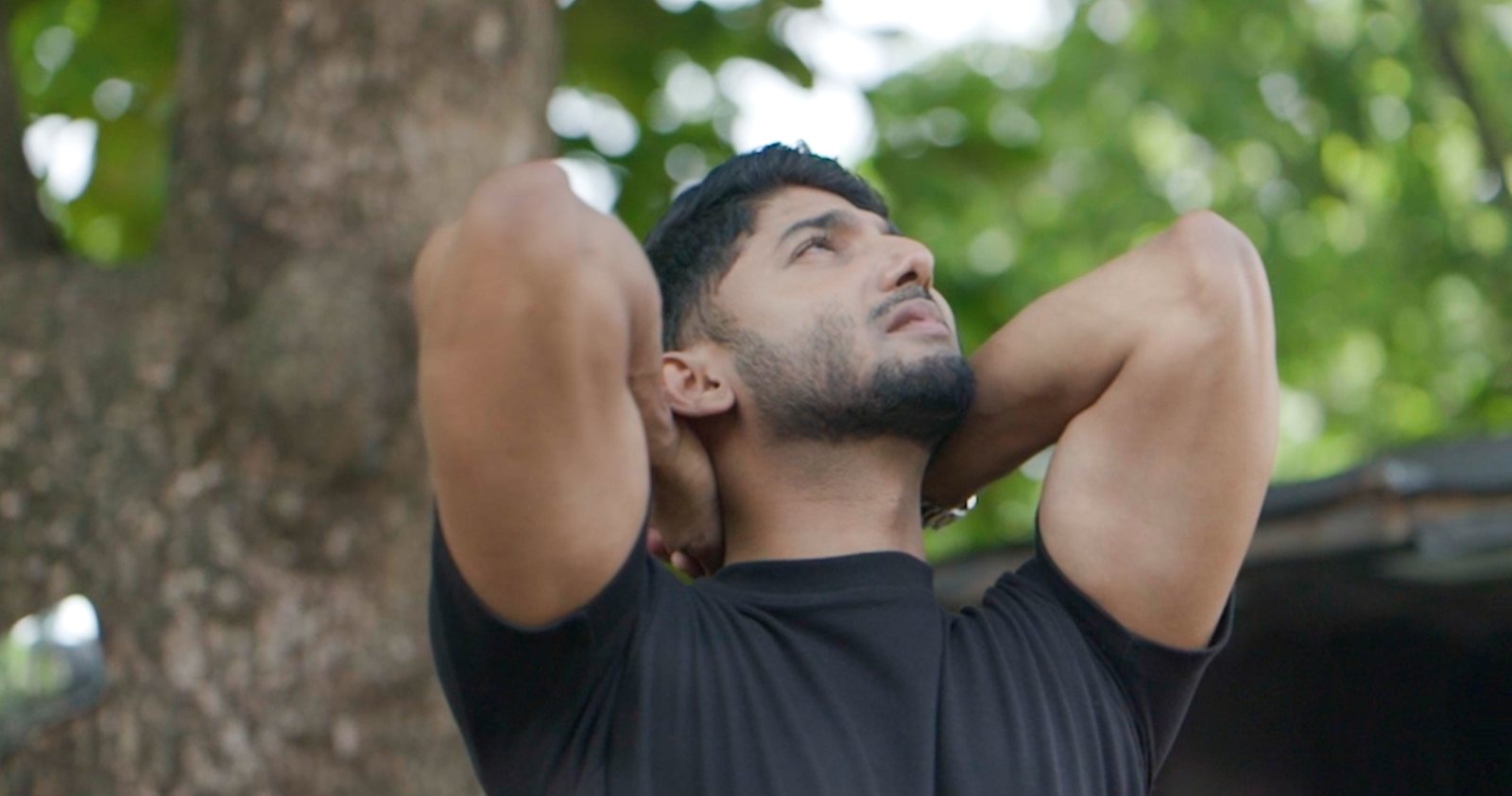 A man outdoors under a tree, looking up
